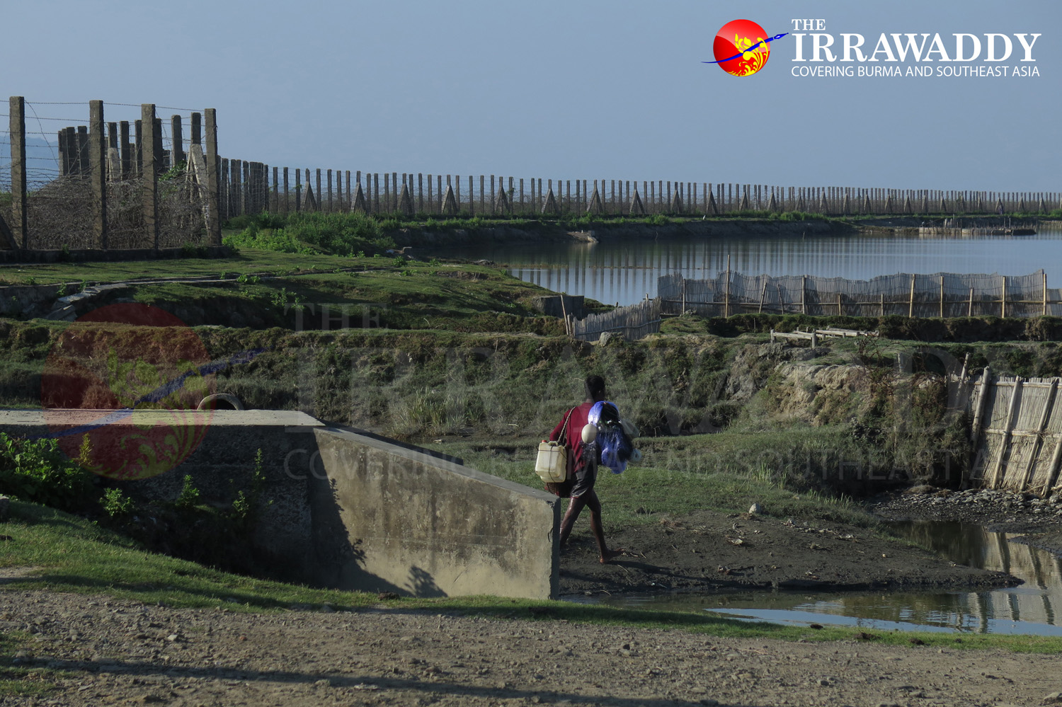 A fisherman walks near the border fence in the western part of Maungdaw town. (Photo: Moe Myint / The Irrawaddy)