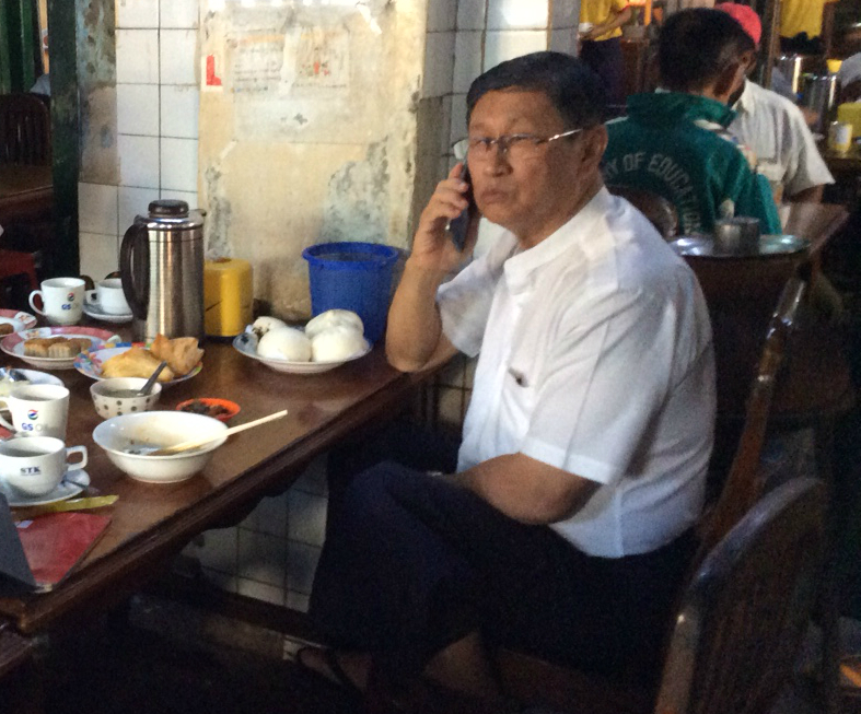 U Aung Htike seen on the phone at the Seit Thine Kya tea shop in June 2016. (Photo: Minka Nijhuis) 